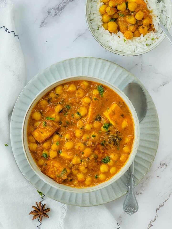 Chana paneer in a white bowl with a spoon in the side.