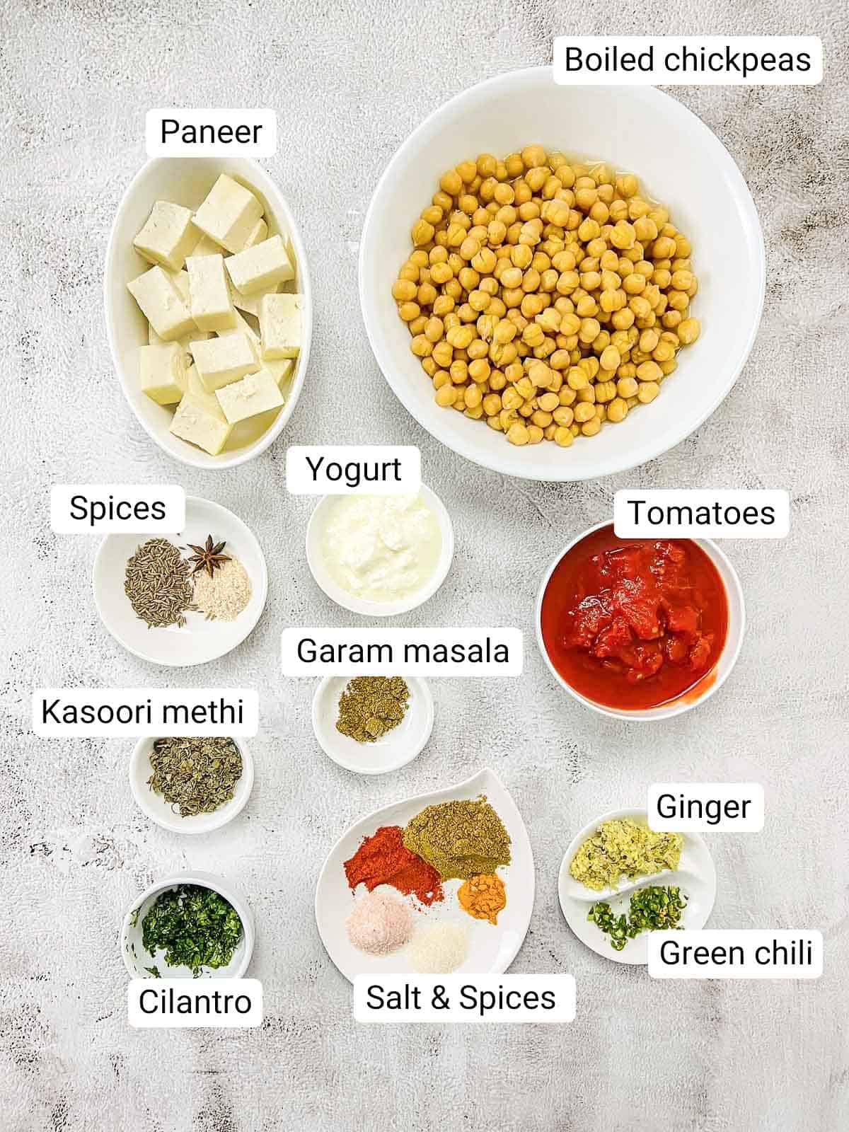 Ingredients to make chana paneer placed on a white surface.