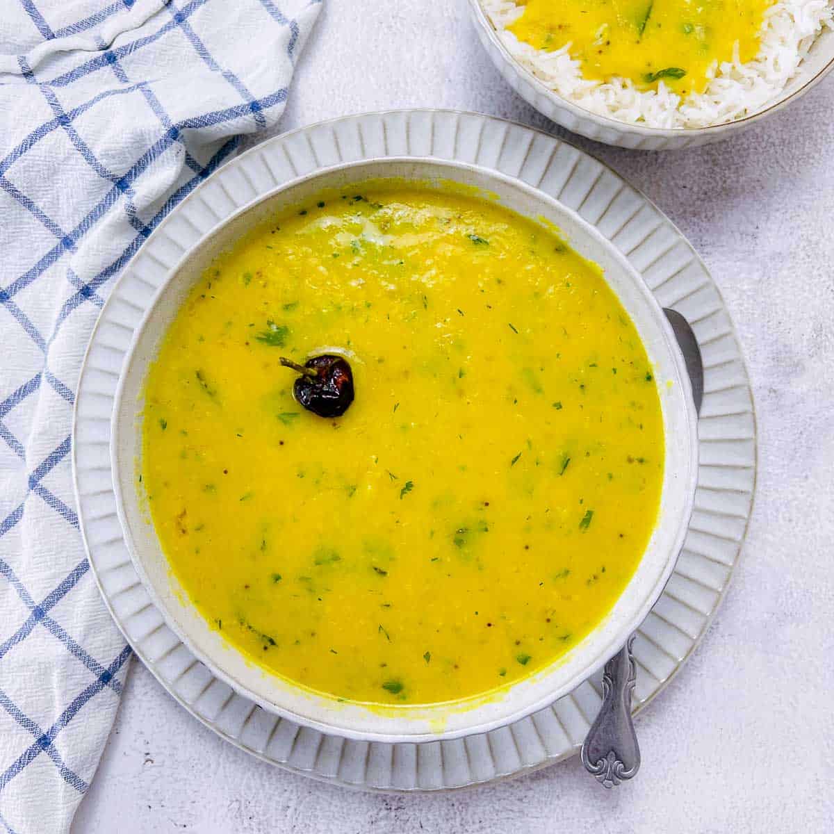 Yellow dal in a white bowl placed on a white surface.