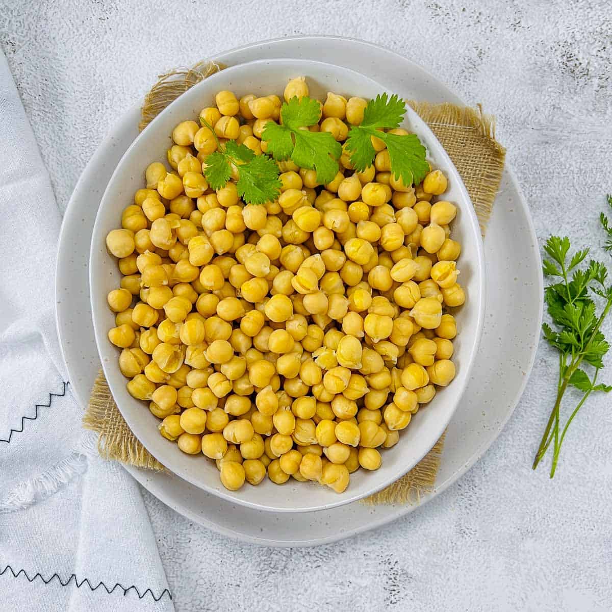 Cooked chickpeas in a white bowl with cilantro in the background.