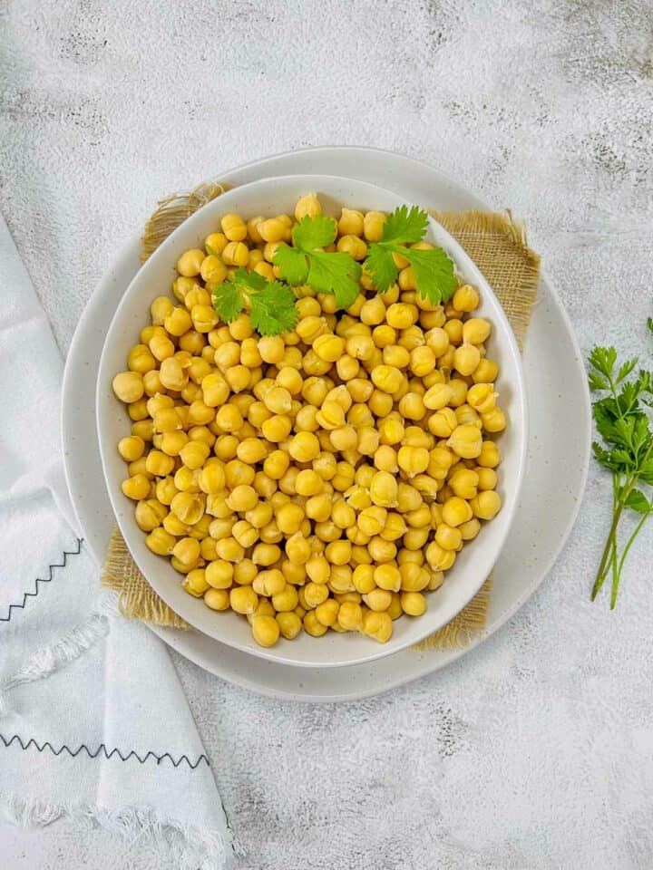Cooked chickpeas in a white bowl placed on white surface.