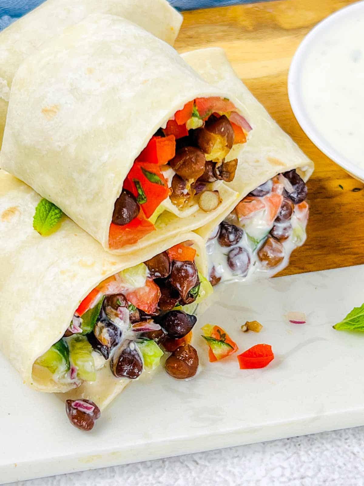 Black chickpea wraps on a wooden board with yogurt sauce in the background.
