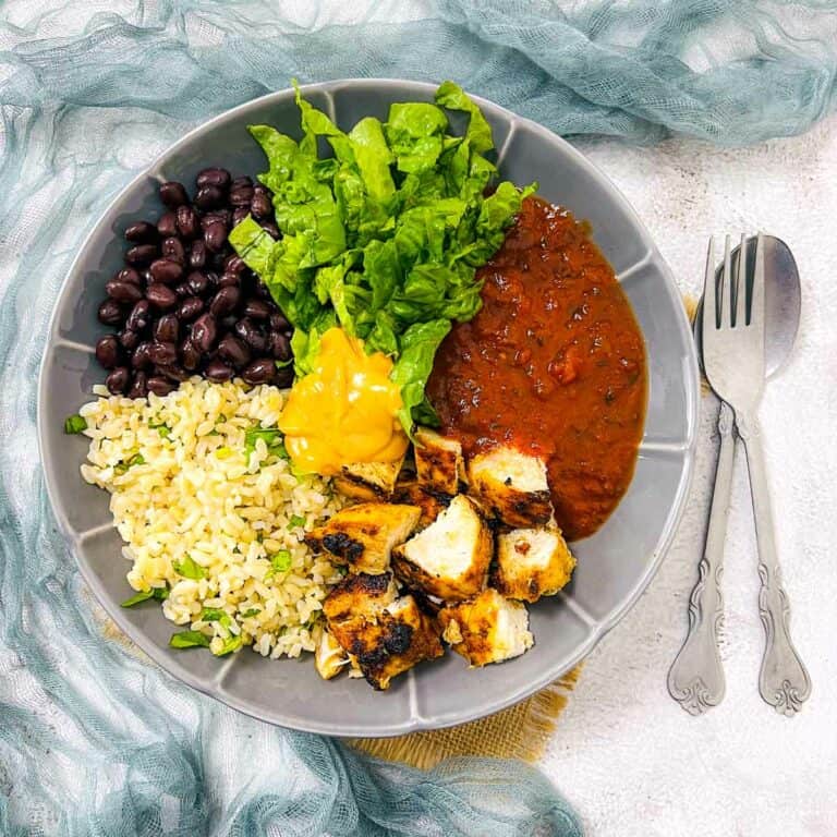 Chicken black bean burrito bowl on a white surface with spoon & fork in the background.