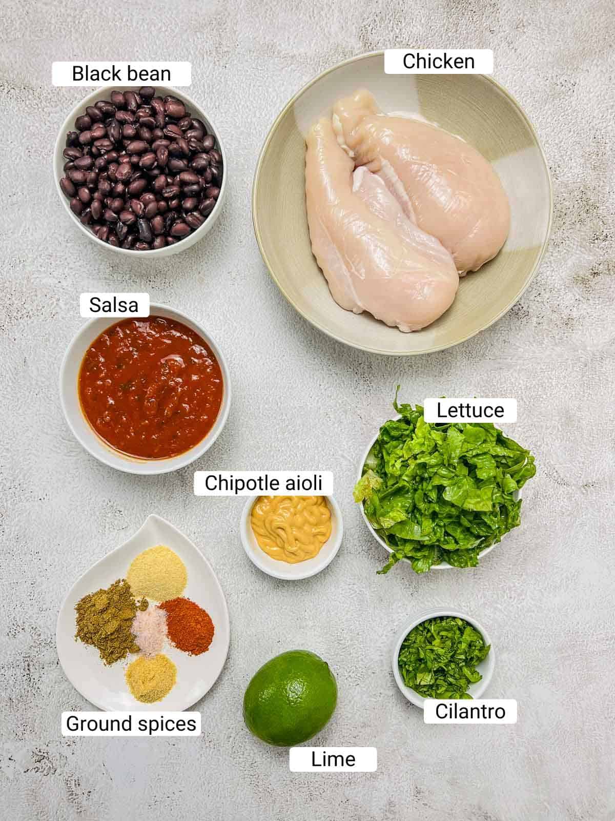 Ingredients to make chicken burrito bowl on a white surface.
