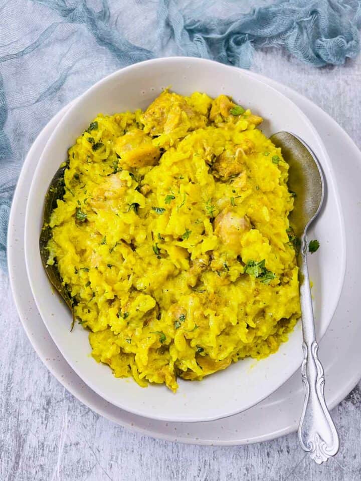 Chicken khichdi in white bowl with a spoon inside.