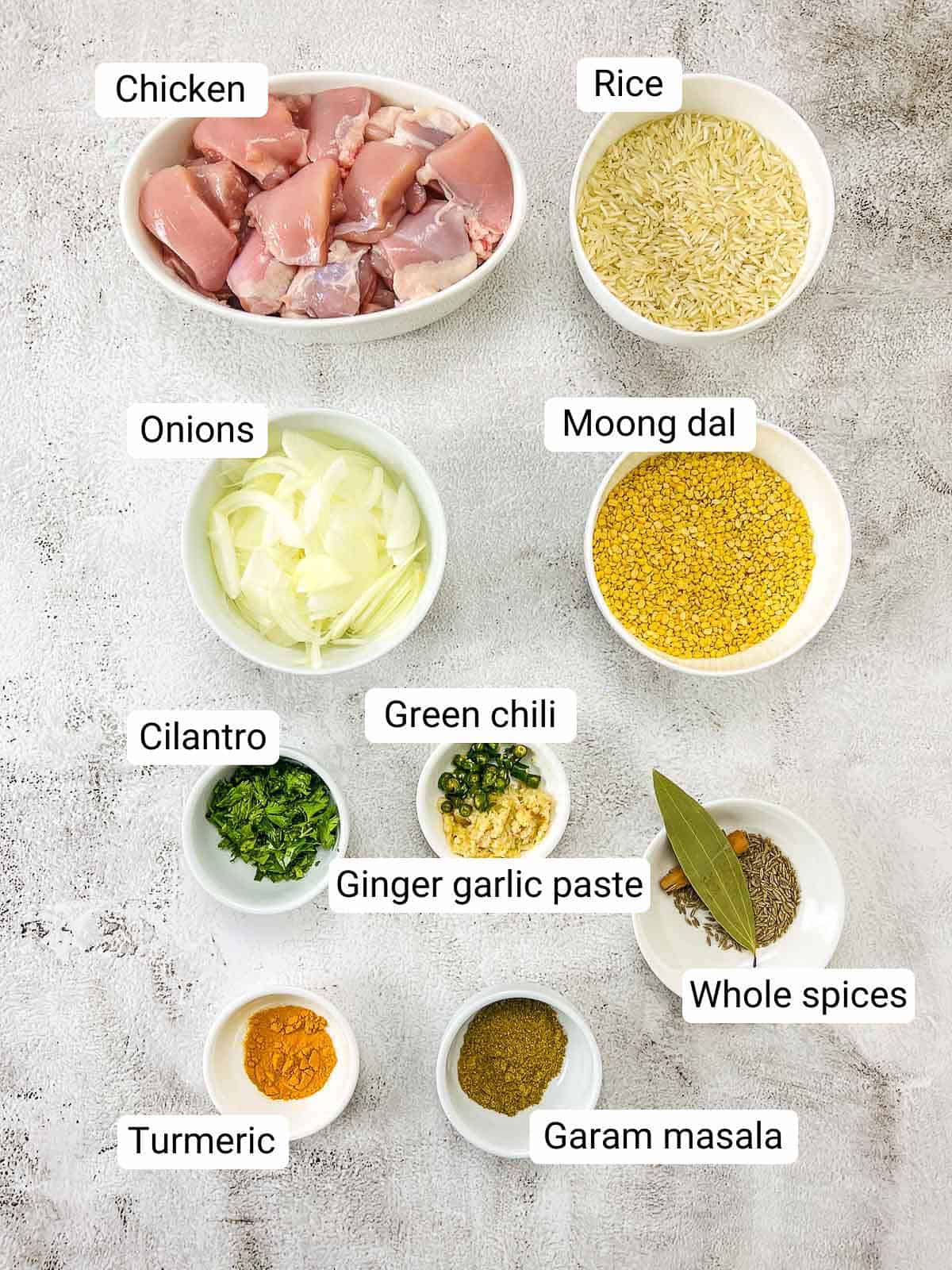 Ingredients to make chicken khichdi placed on a white surface.