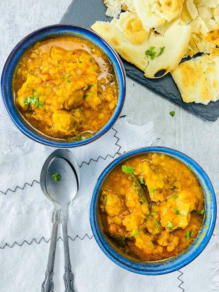 Two bowls of chicken red lentil curry served with naan bread.