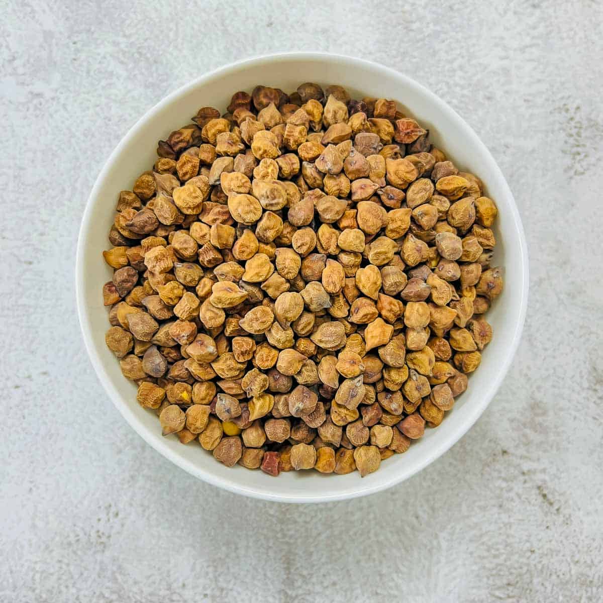 Dried black chickpeas in a white bowl.