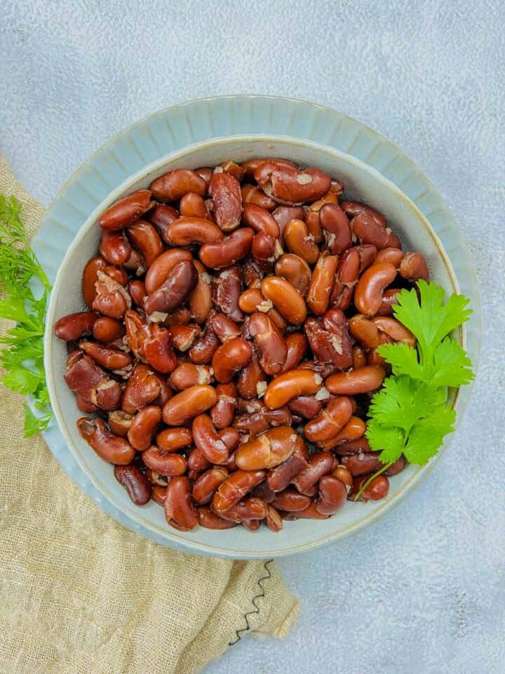 A bowl of cooked kidney beans placed on a white surface with cilantro in the background.