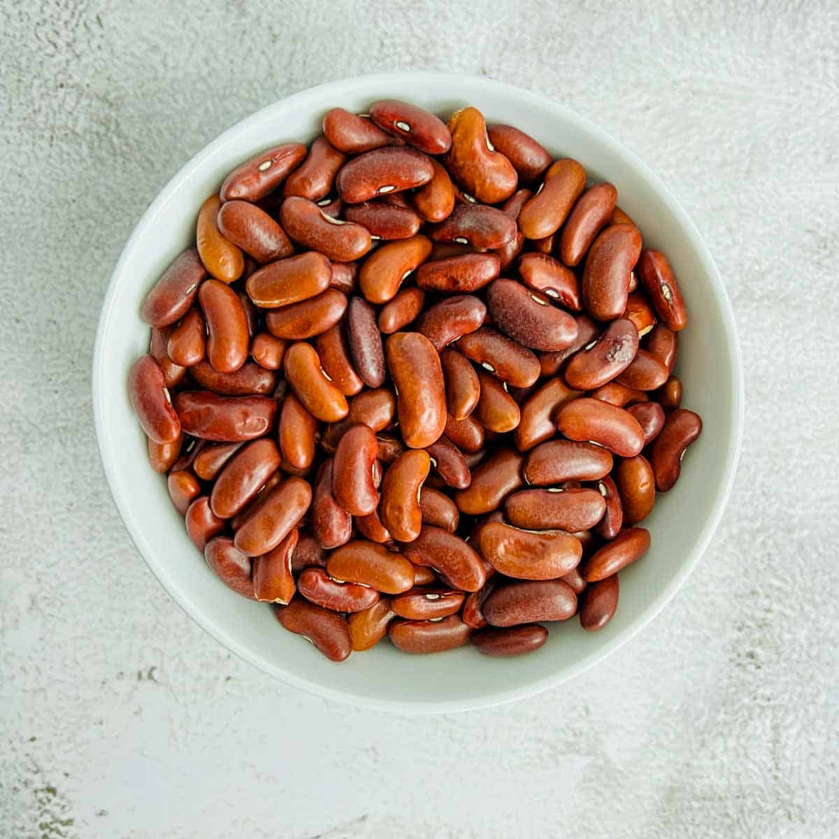 Dried kidney beans in a white bowl placed on a white surface.