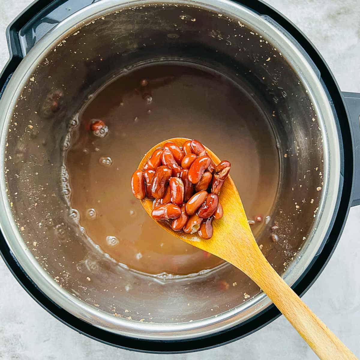 Cooked beans on a wooden spoon over the Instant Pot.