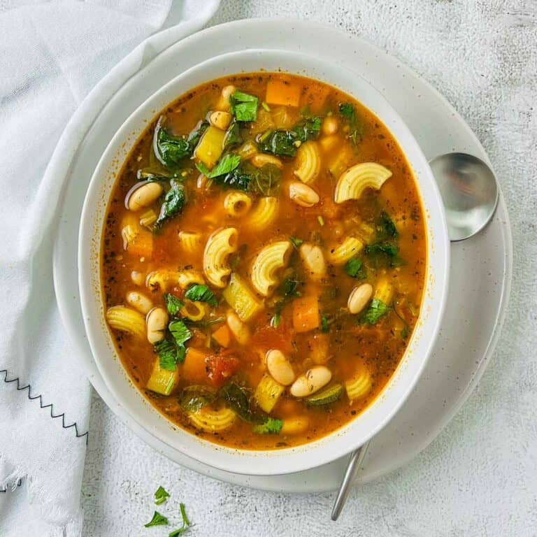 Minestrone soup in a white bowl with a soup spoon in the background.