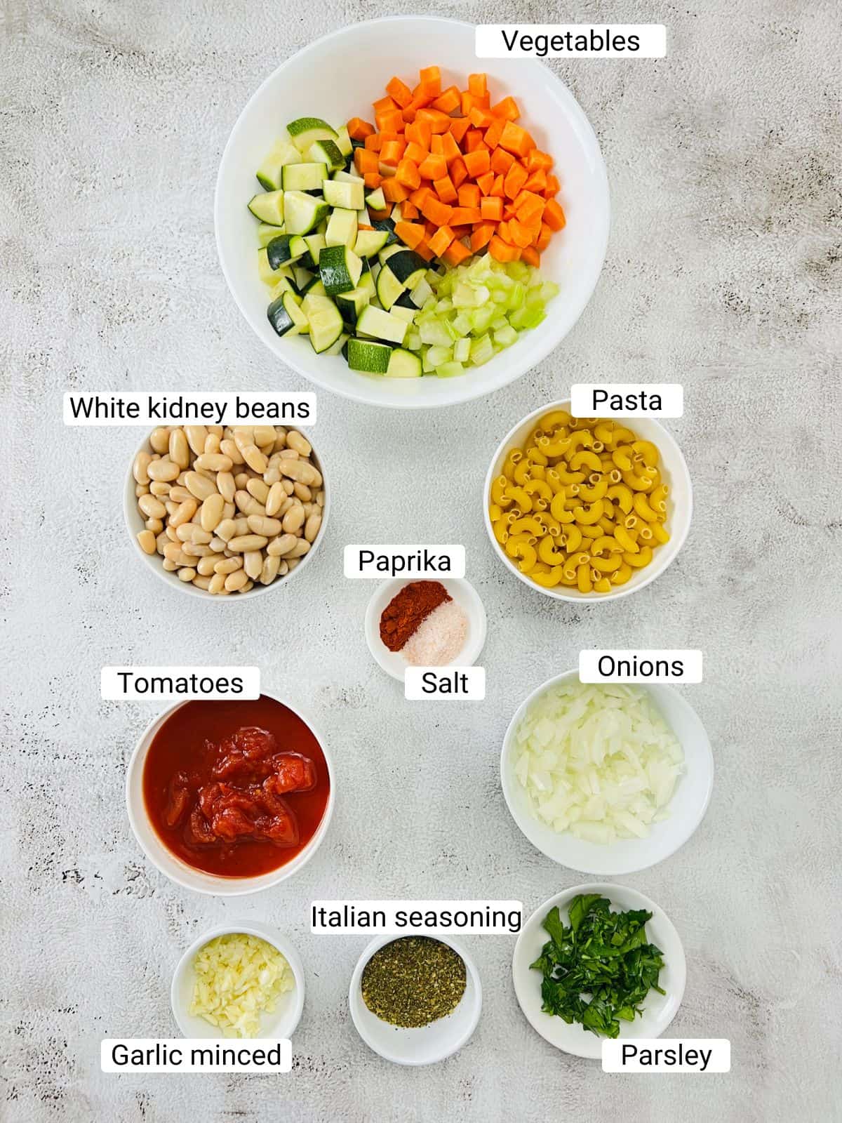 Ingredients to make minestrone soup on a white surface.