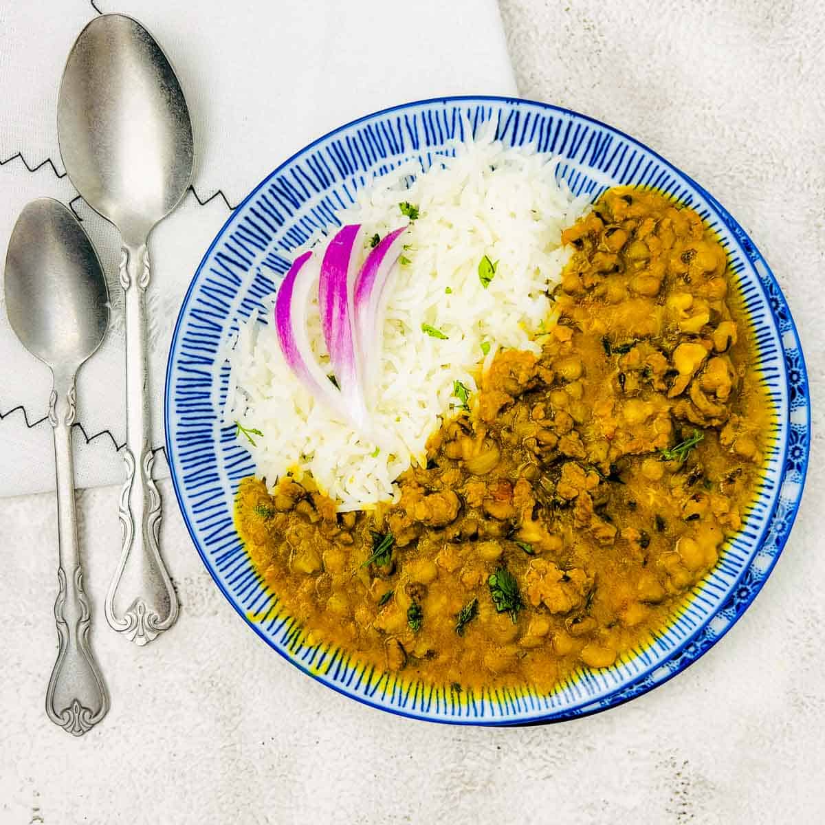 Keema green moong curry with steamed rice and onion slices on blue plate.