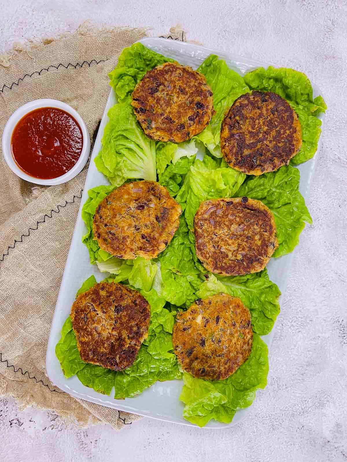 Kidney bean patties and lettuce leaves on white plate.