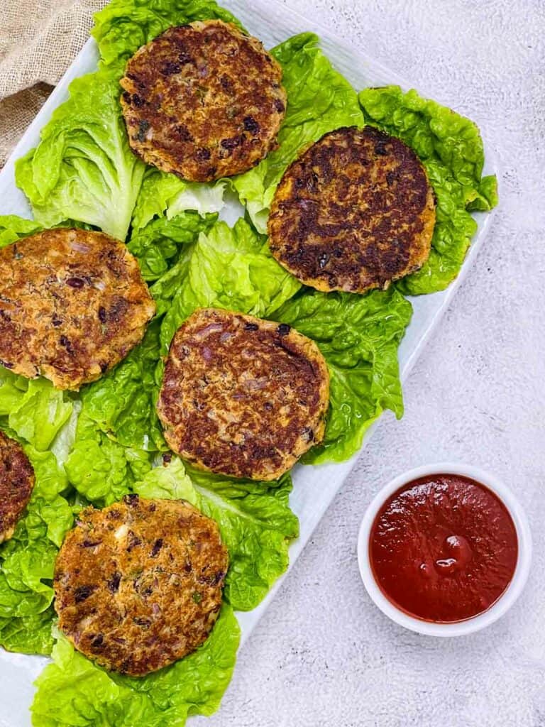 Kidney bean patties on a bed of lettuce with ketchup in the side.