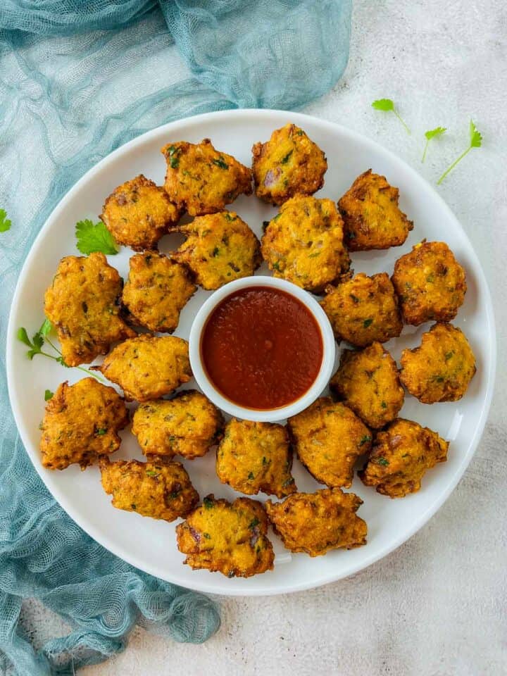 Red lentil fritters in a white plate with cilantro garnish and ketchup in a white bowl.