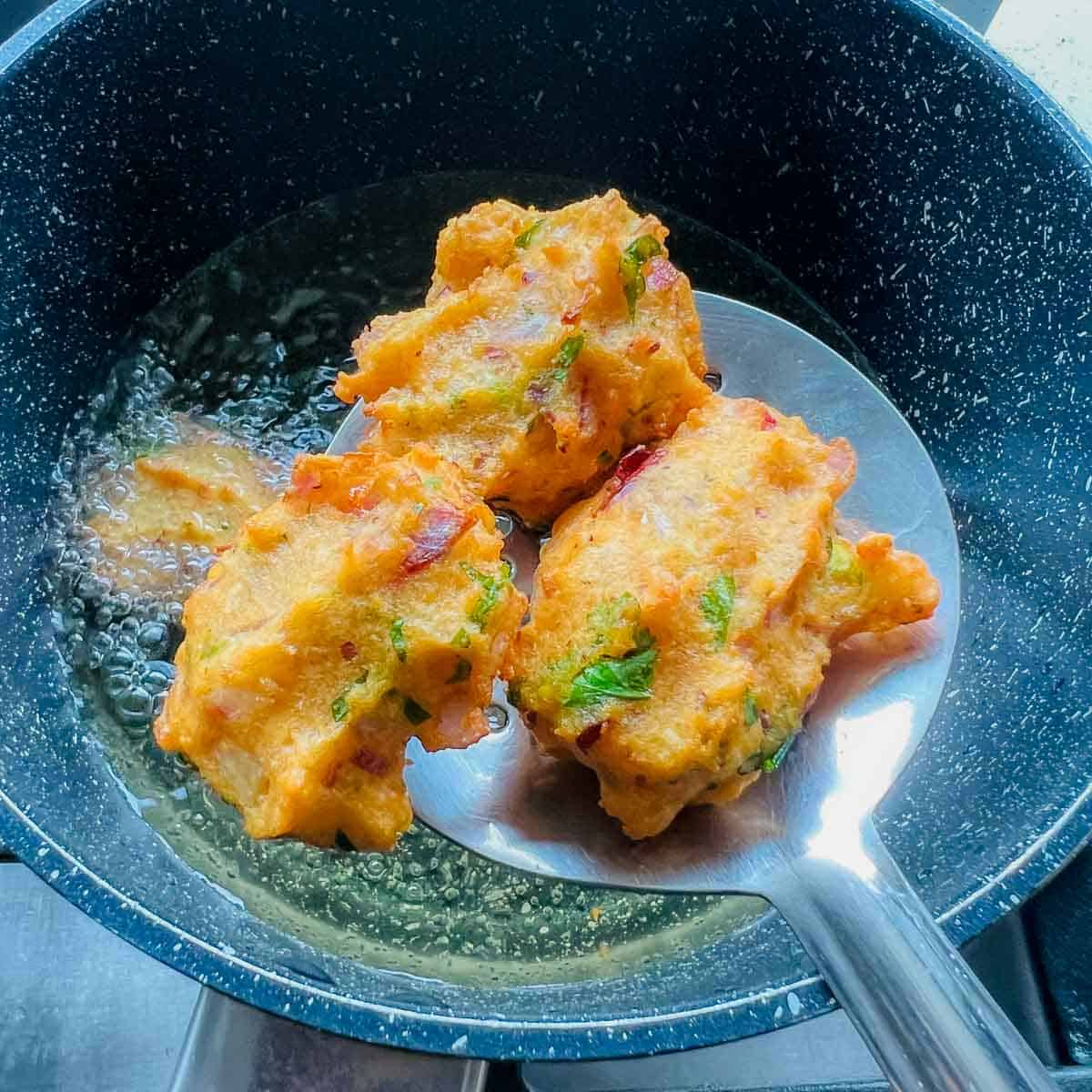 Deep fried fritters on a slotted spoon.