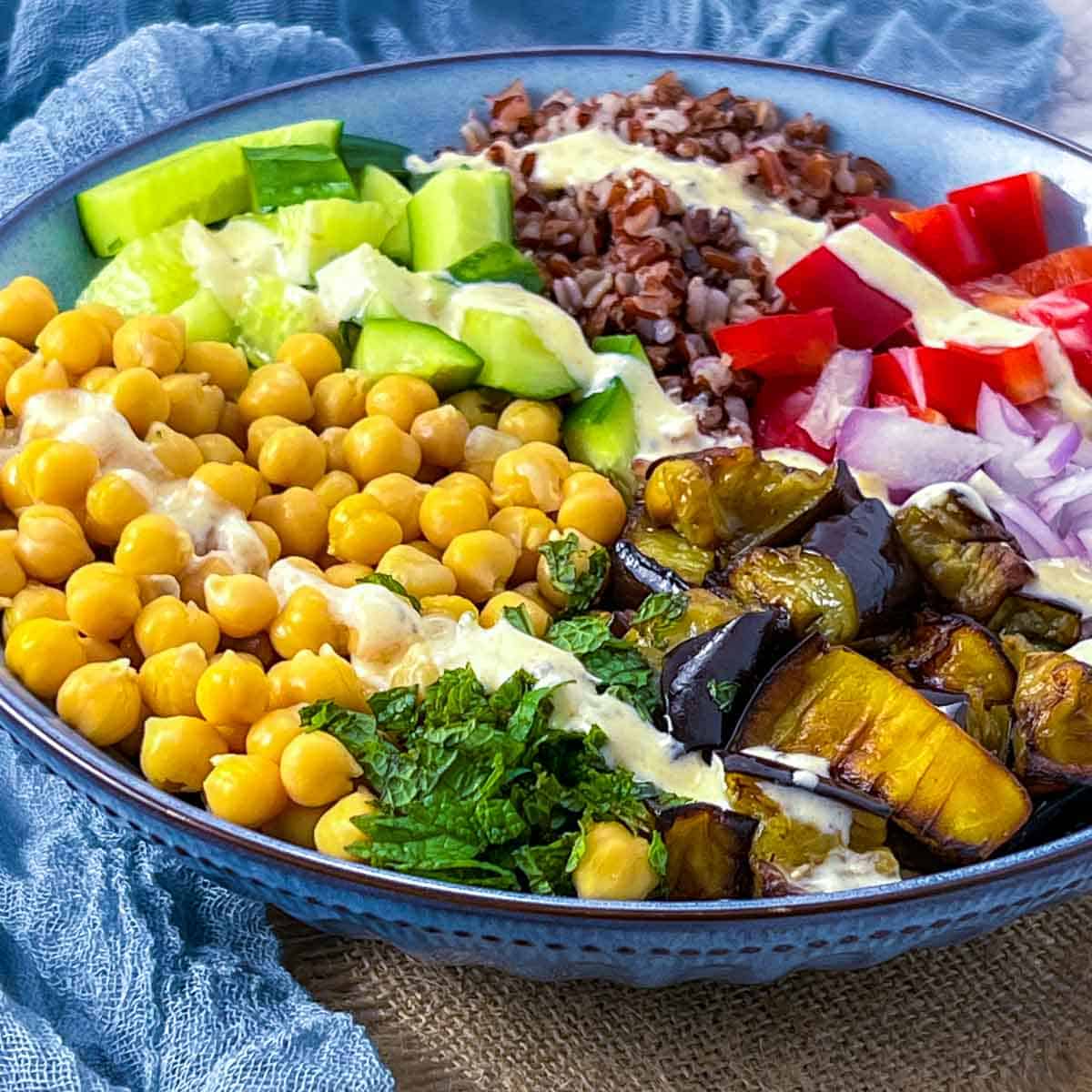 Eggplant and chickpea Buddha bowl drizzled with yogurt sauce on top.