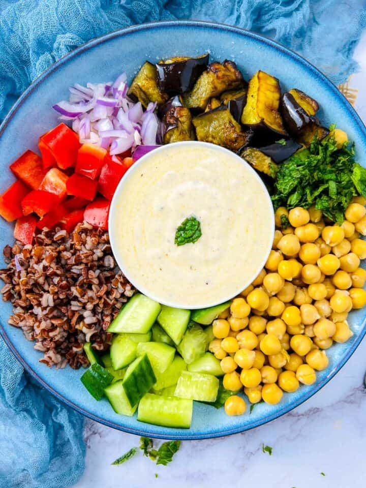 Roasted eggplant and chickpea buddha bowl with yogurt sauce in the center.