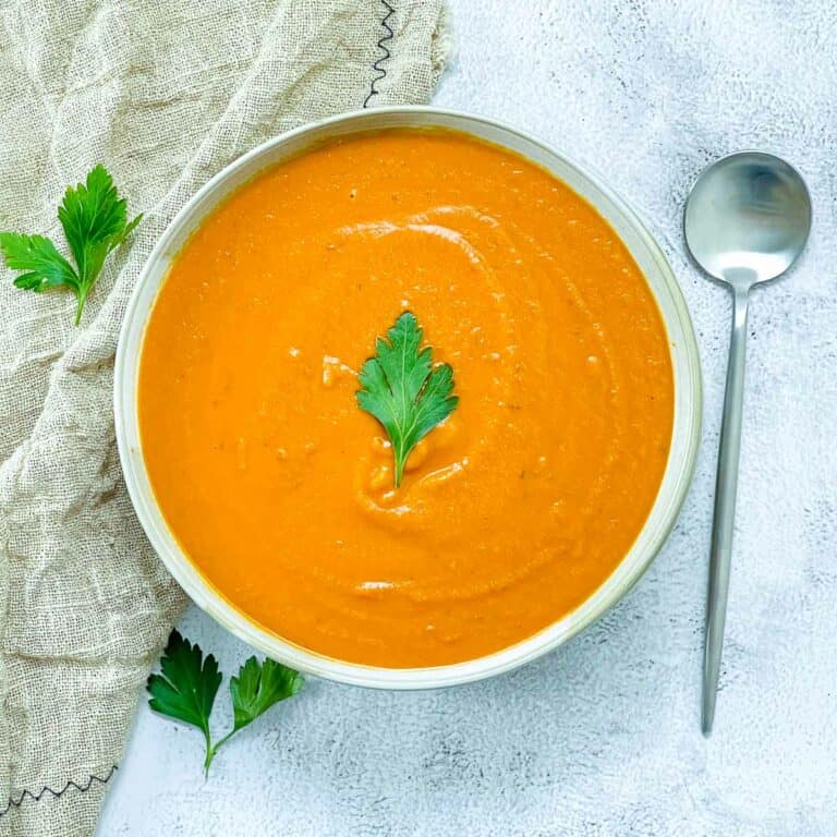A bowl of tomato lentil soup topped with parsley on a white surface.