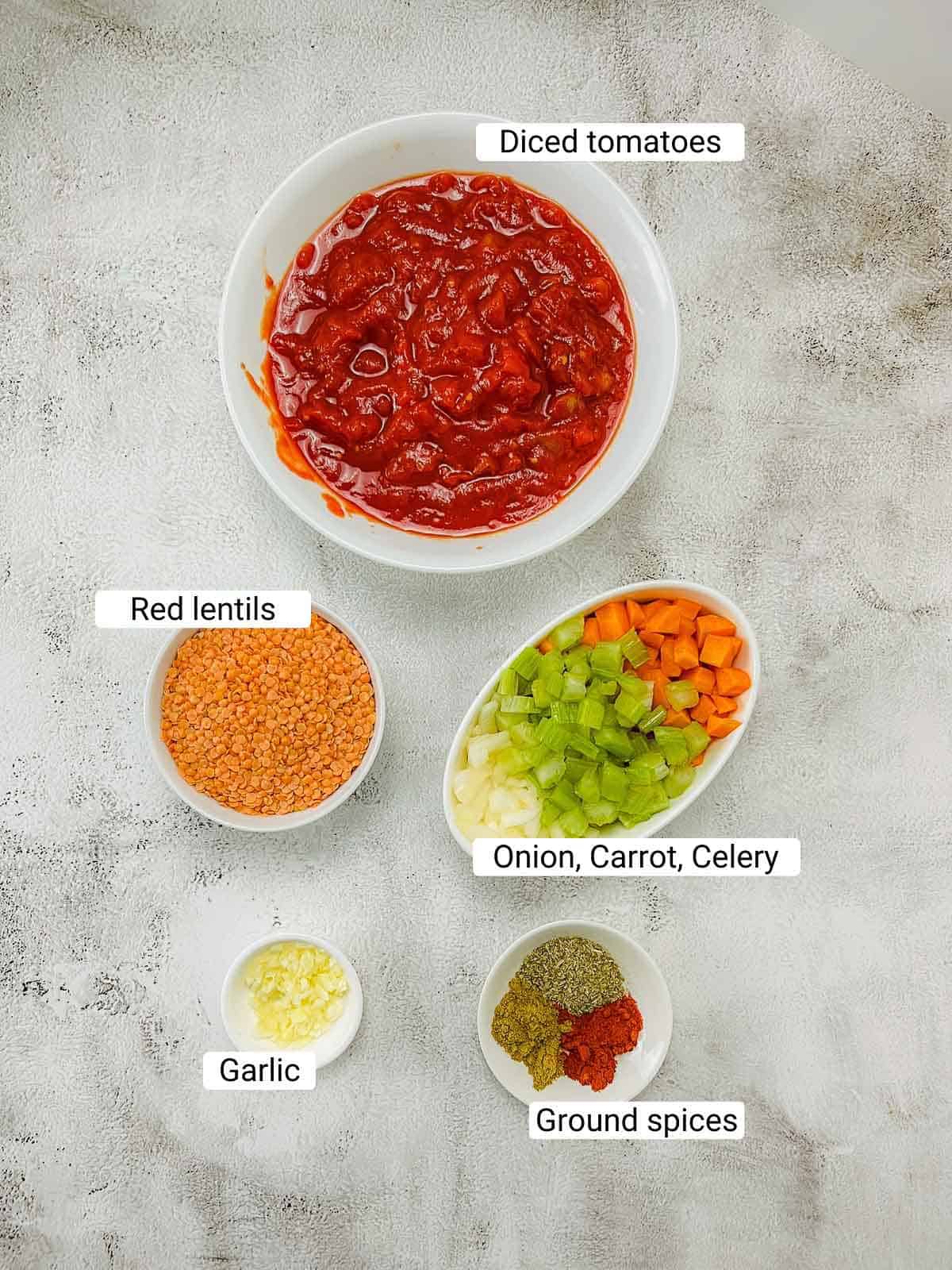 Ingredients to make tomato lentil soup on a white surface.