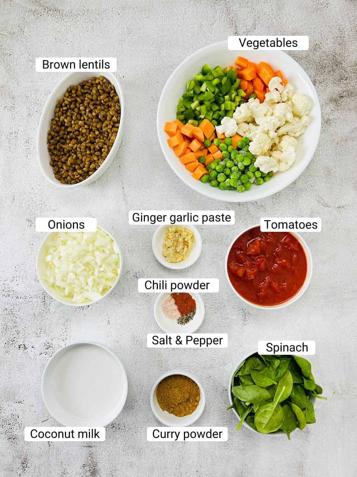 Ingredients to make vegetable lentil curry placed on a white surface.