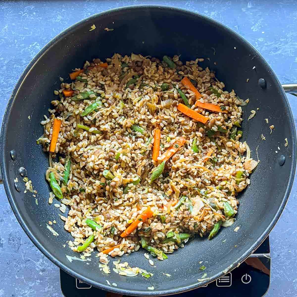 Rice, lentils, and sauces tossed with veggies in the frying pan.
