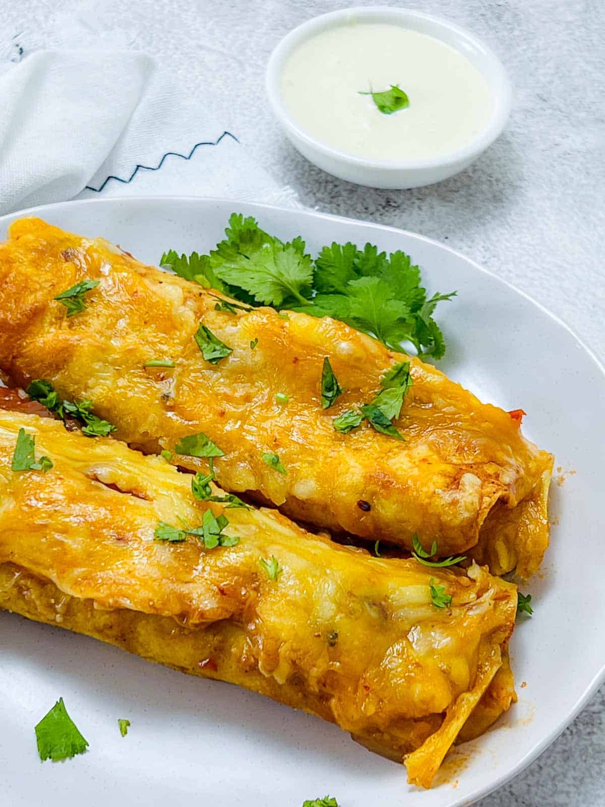 Chicken lentil enchiladas on a white plate with sour cream in the background.