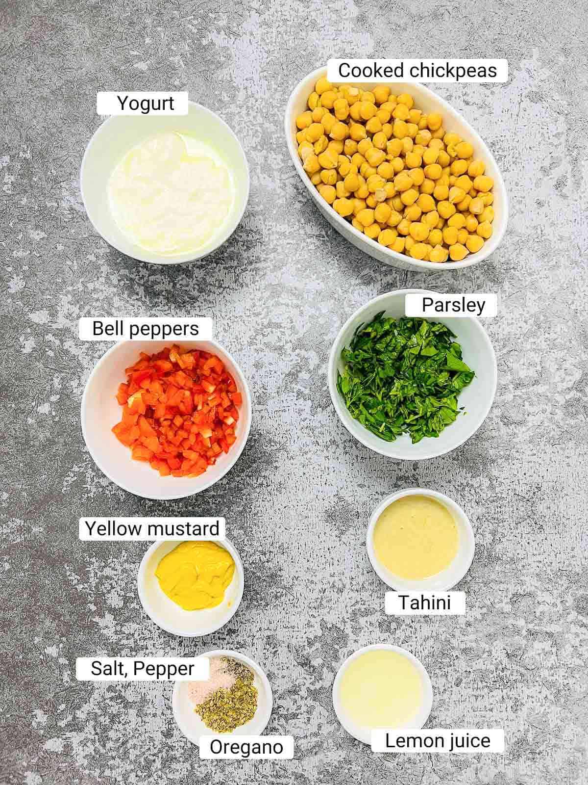 Ingredients to make chickpea salad sandwich on a grey surface.