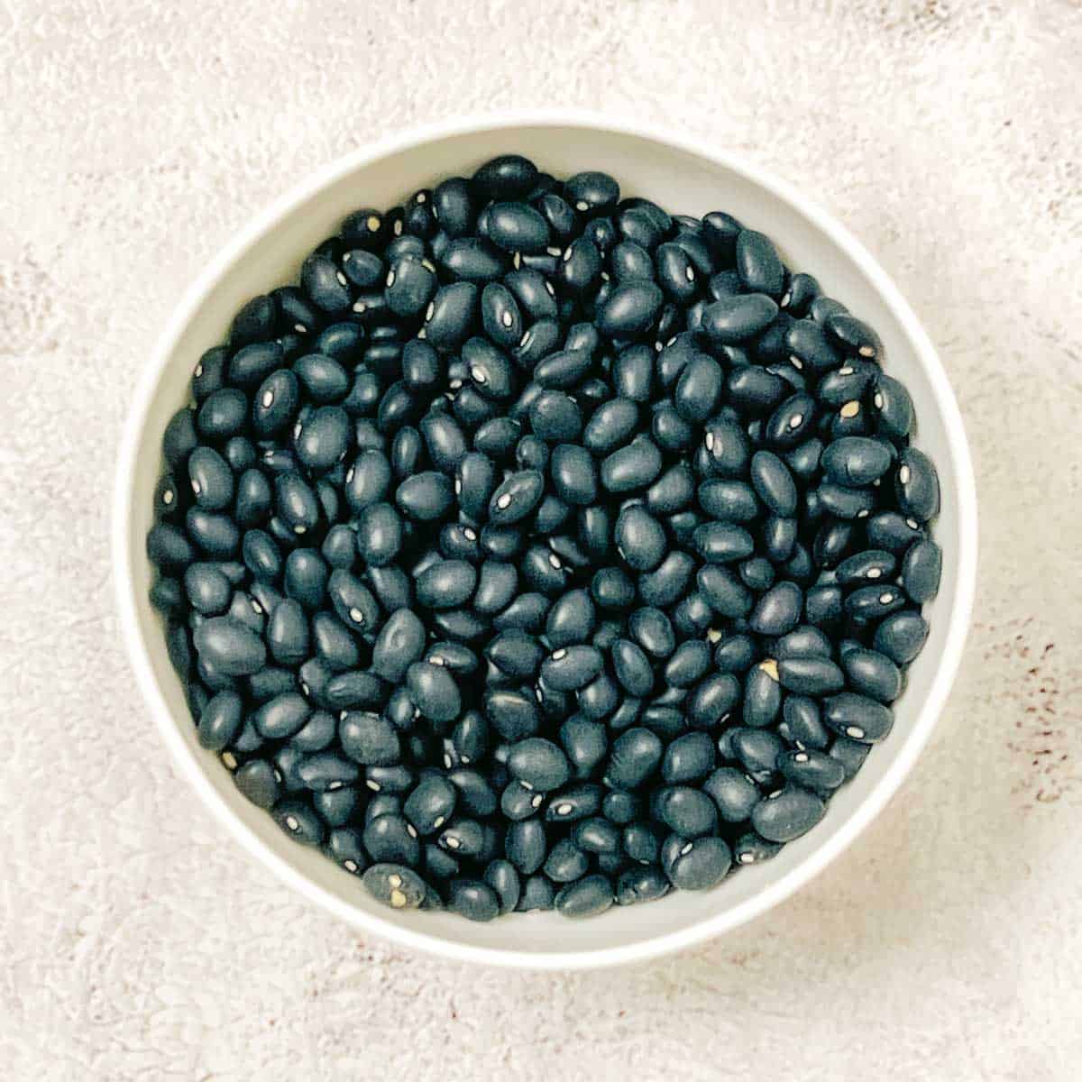 Uncooked dried black beans in a white bowl.