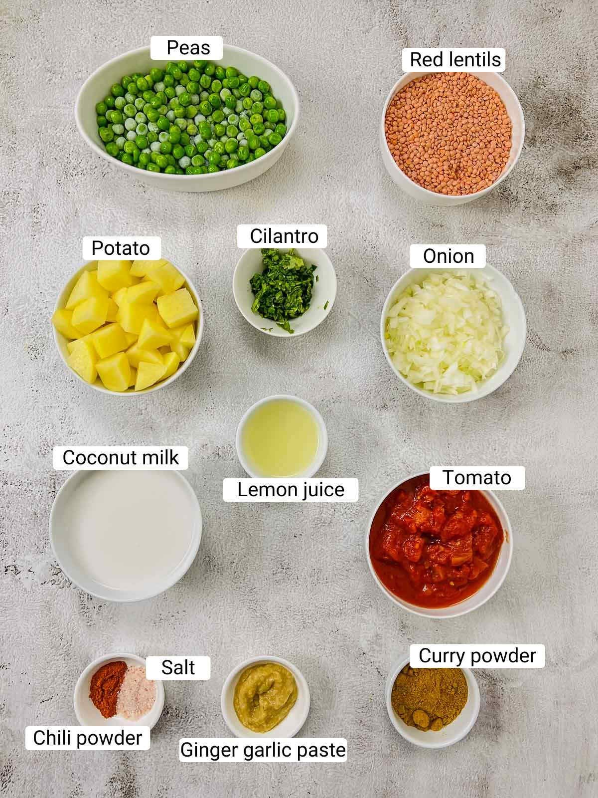 Ingredients to make lentil peas potato curry on a white surface.