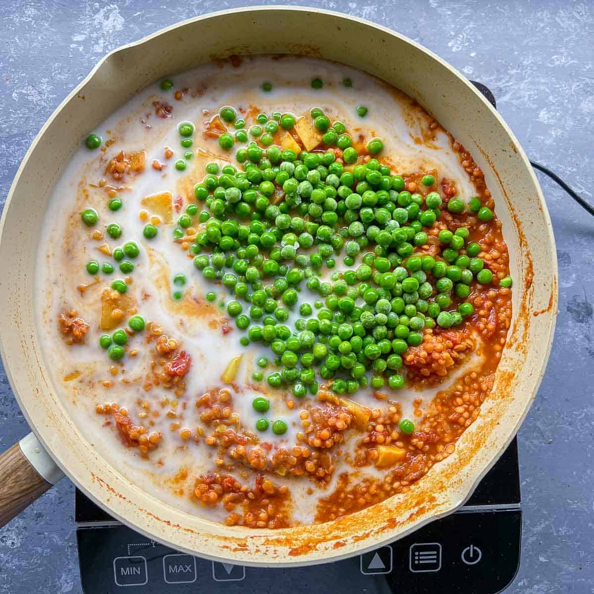 Coconut milk and peas added to the frying pan.