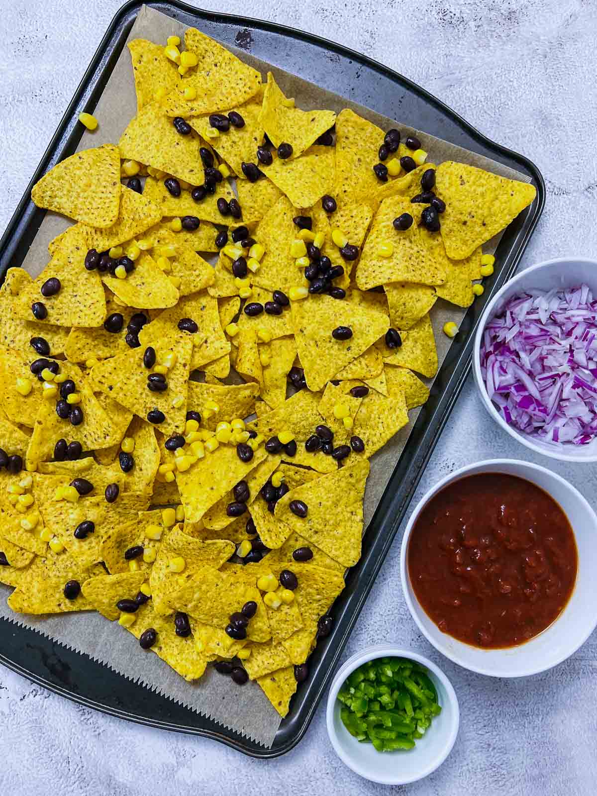 Nachos spread on baking sheet and topped with black beans and corn.