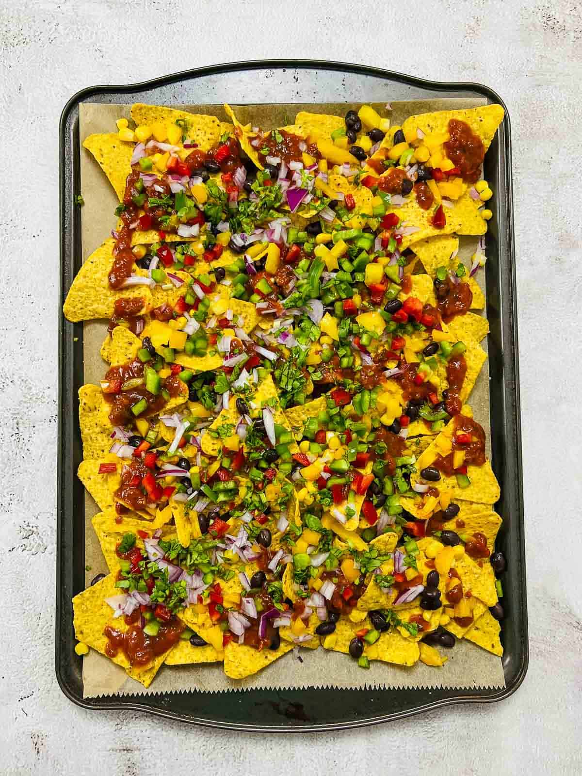 Chopped veggies and salsa added as toppings on nachos.