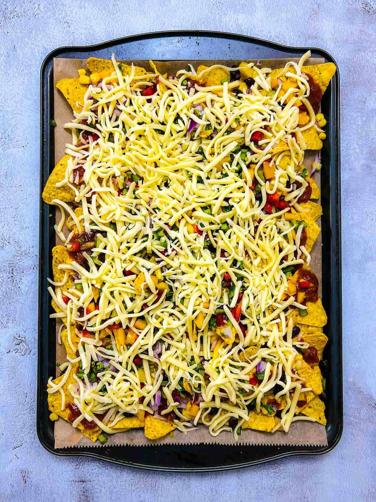 Nachos topped with shredded cheese before putting into the oven.