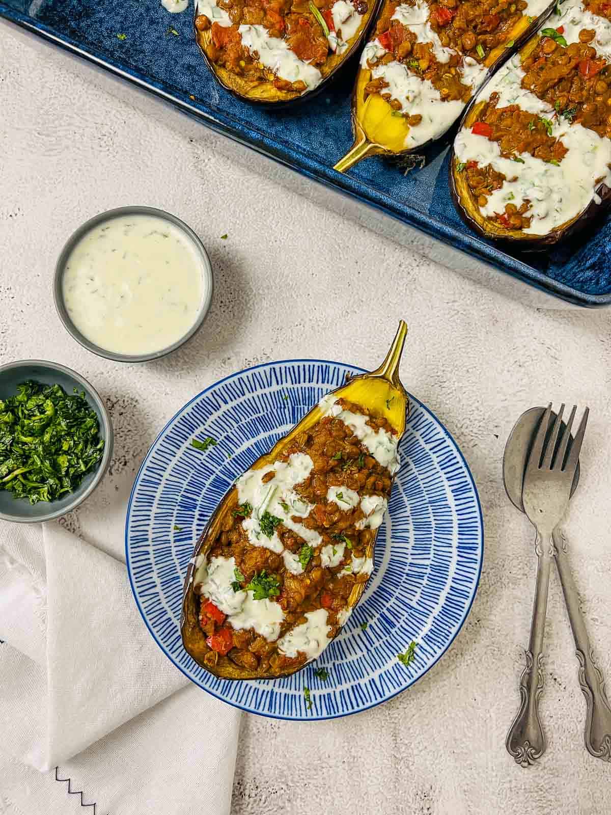 A slice of lentil stuffed eggplant on a blue plate with baking dish in the background.