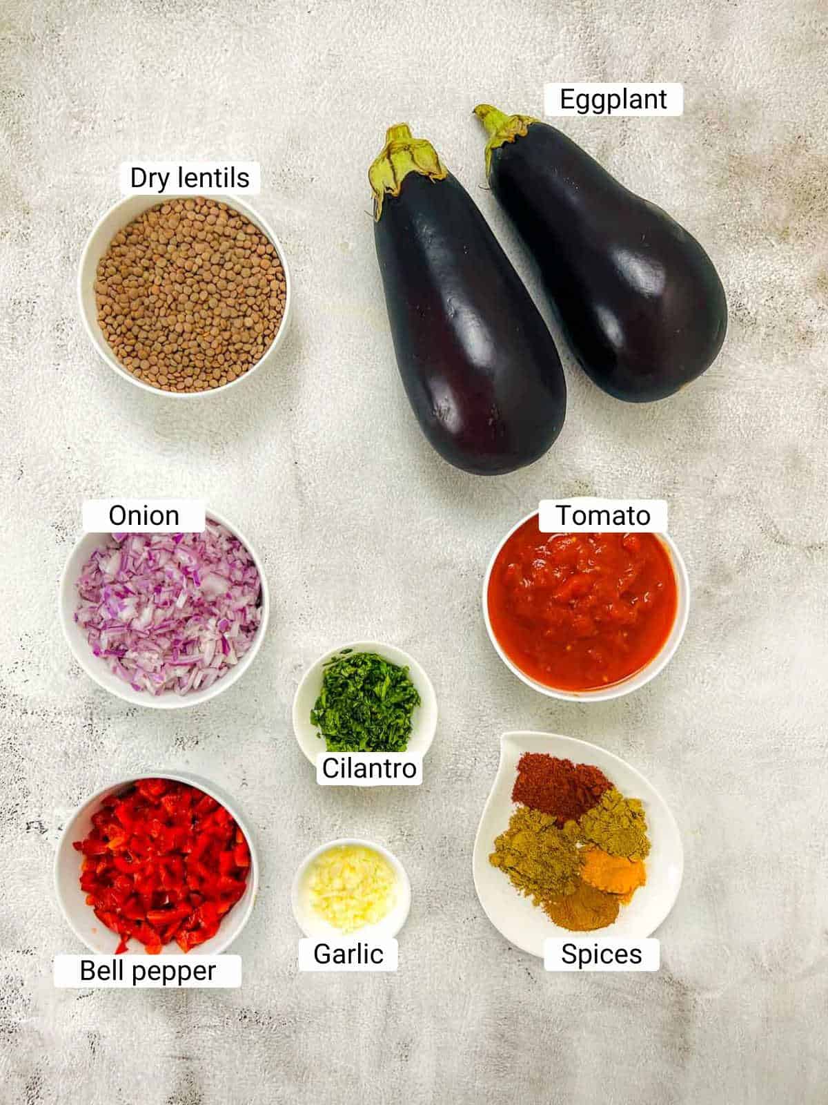 Ingredients to make lentil stuffed eggplants on a white surface.