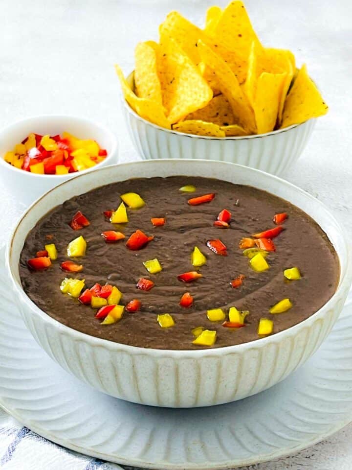 Refried beans in a white bowl with tortilla chips in the background.