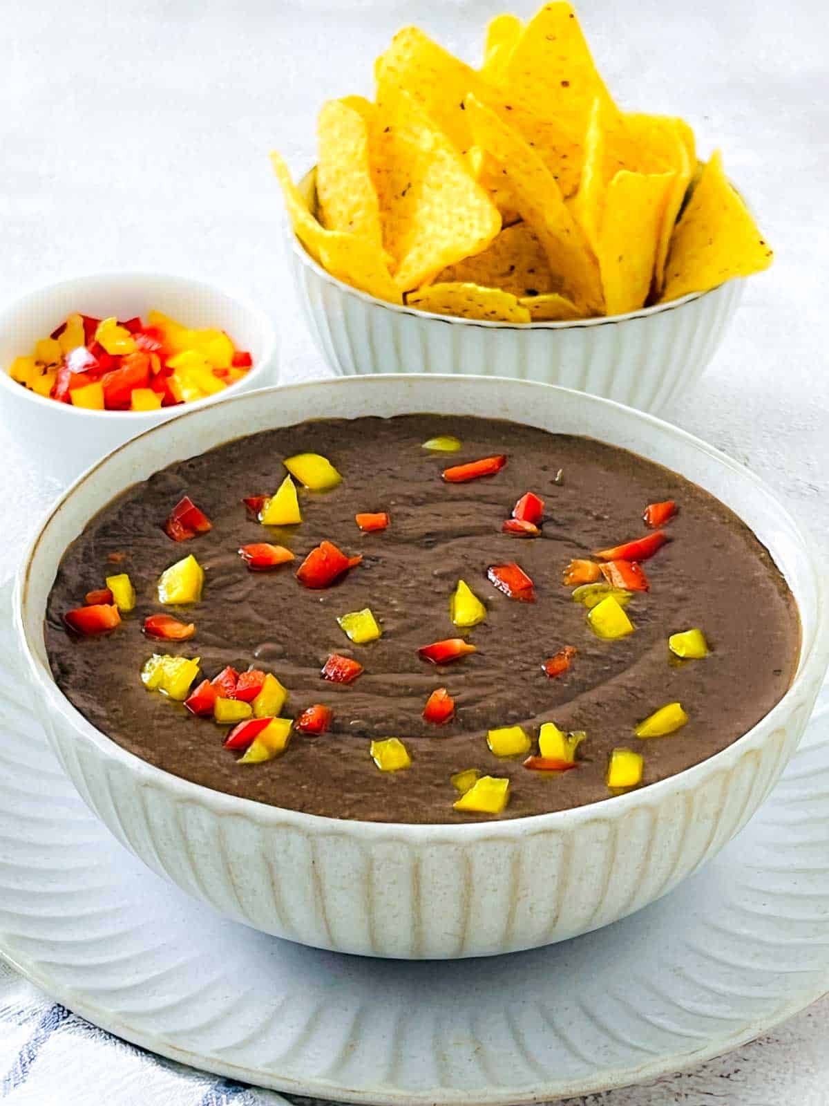 Refried beans in a white bowl with tortilla chips in the background.