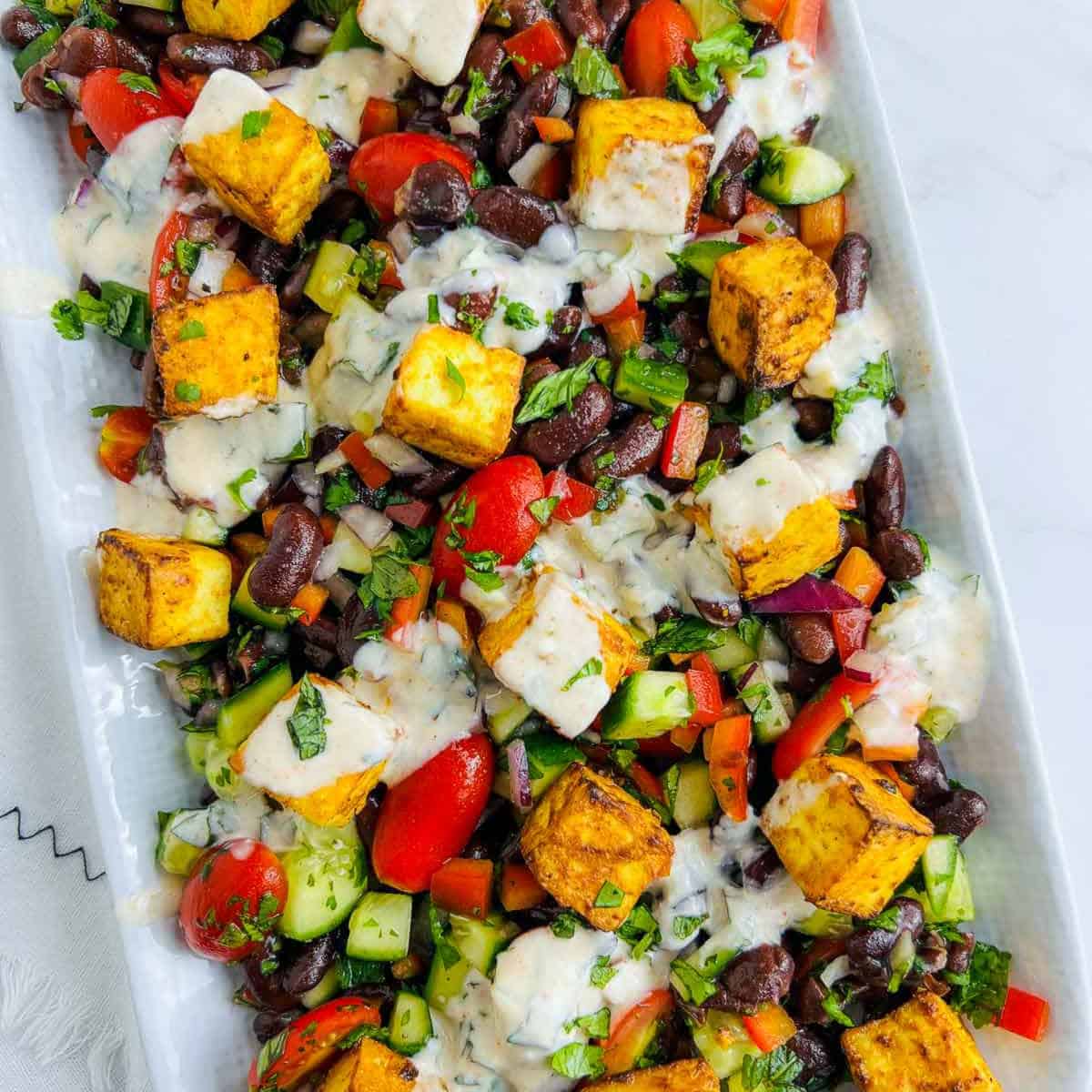 Assembling salad with paneer and dressing.