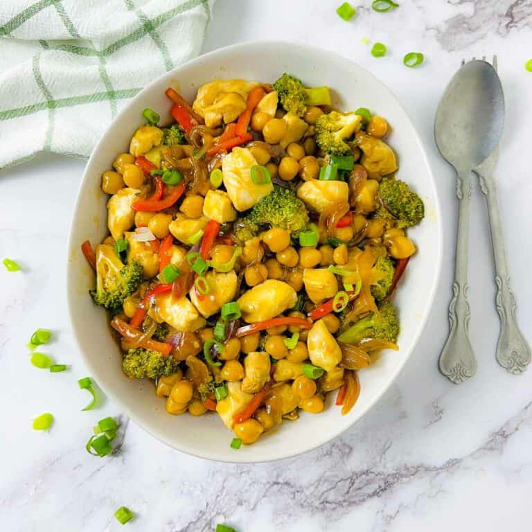 Chicken chickpea stir fry in a white bowl with spoons in the background.