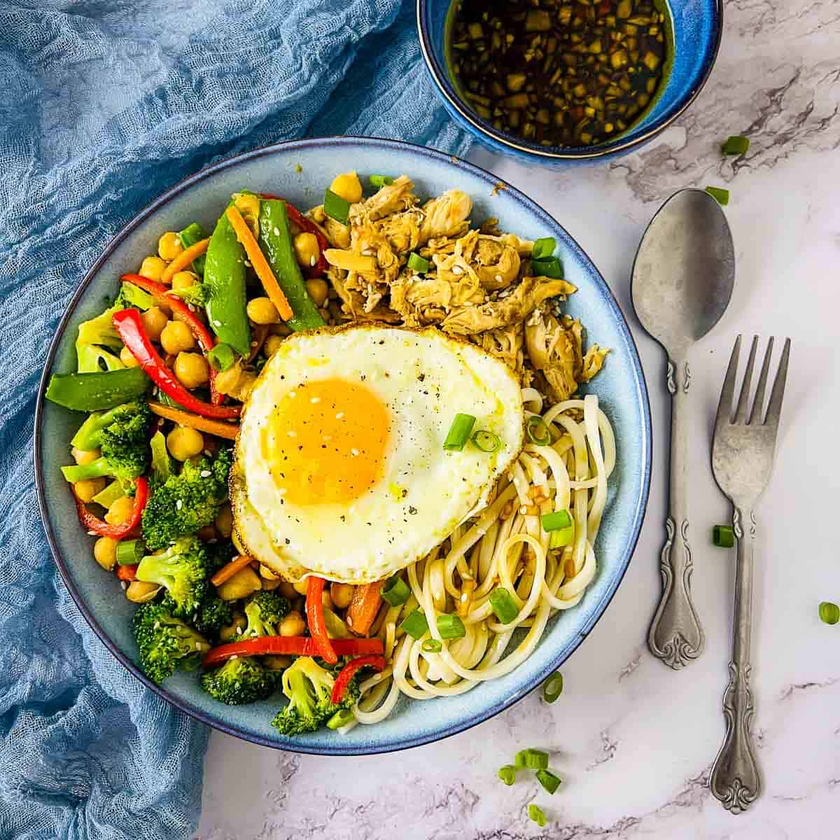 Chicken and chickpea udon noodle bowl topped with fried egg.