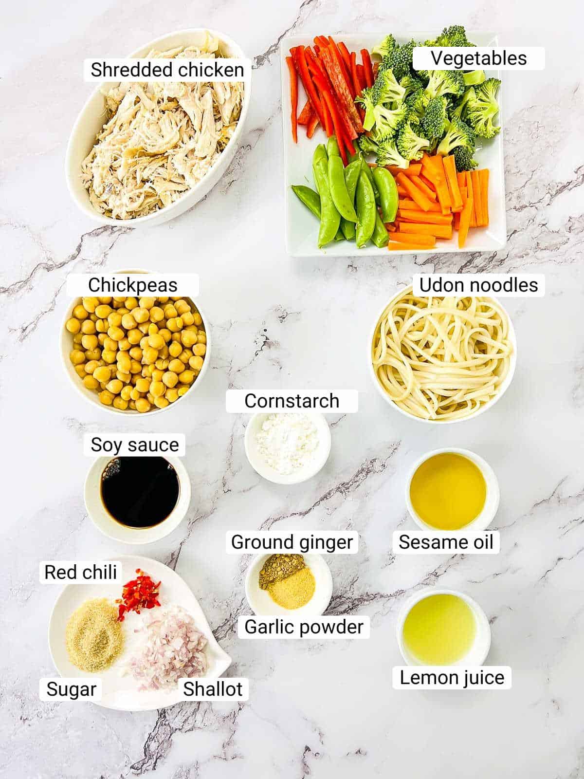 Ingredients to make chicken and chickpea udon noodle bowl on a white surface.