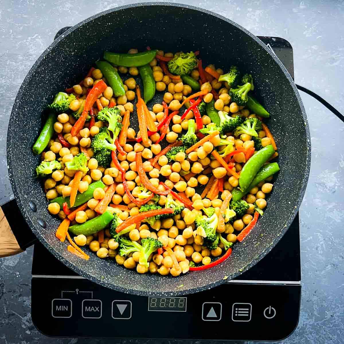 Veggies, chickpeas, and spices sauted in a frying pan.