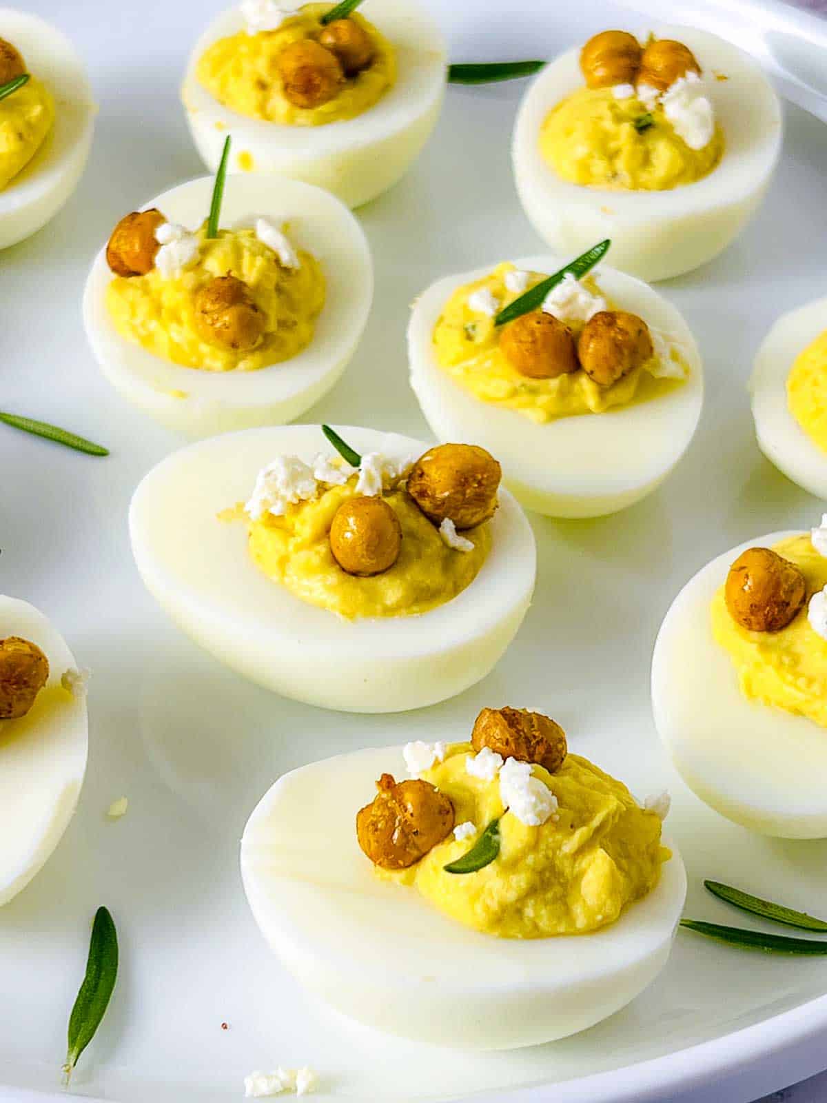 Deviled eggs topped with crumbled feta, roasted chickpeas, and fresh rosemary.