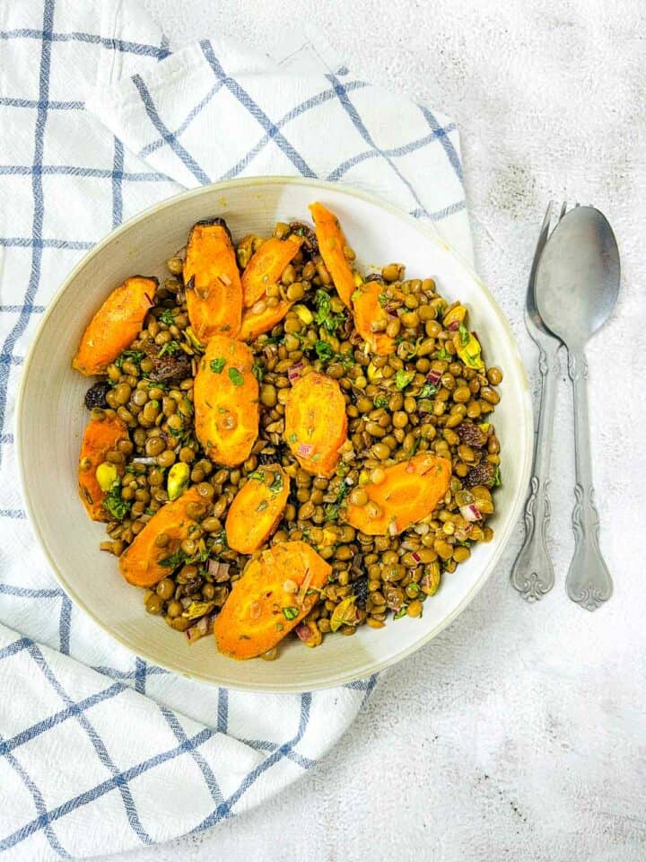 Moroccan lentil and carrot salad in a white bowl with spoons in the background.