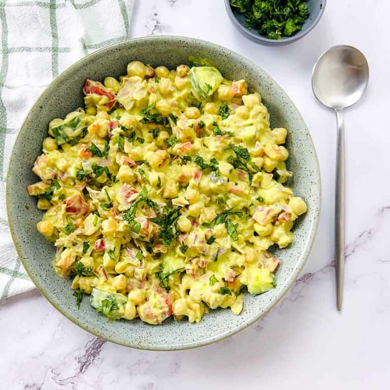 Tuna chickpea salad with avocado dressing in a green bowl with a spoon on the side.