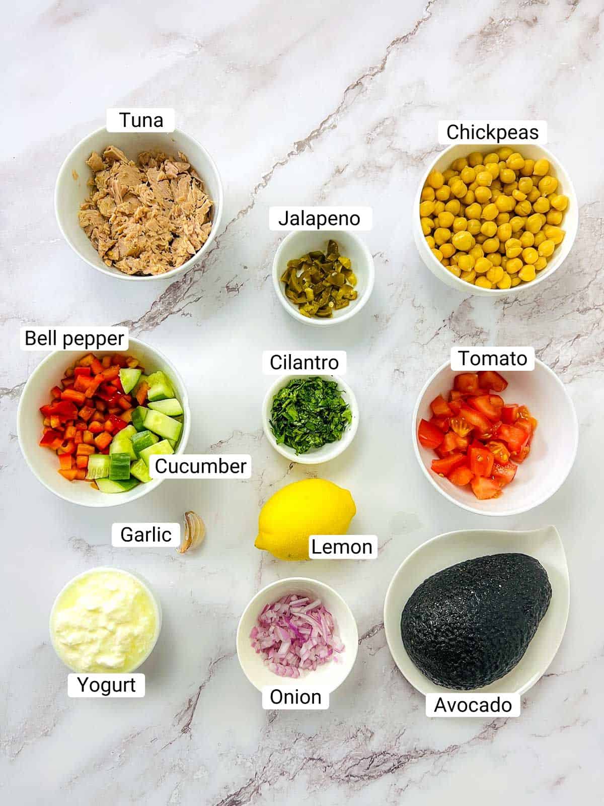 Ingredients to make tuna chickpea salad on a white surface.