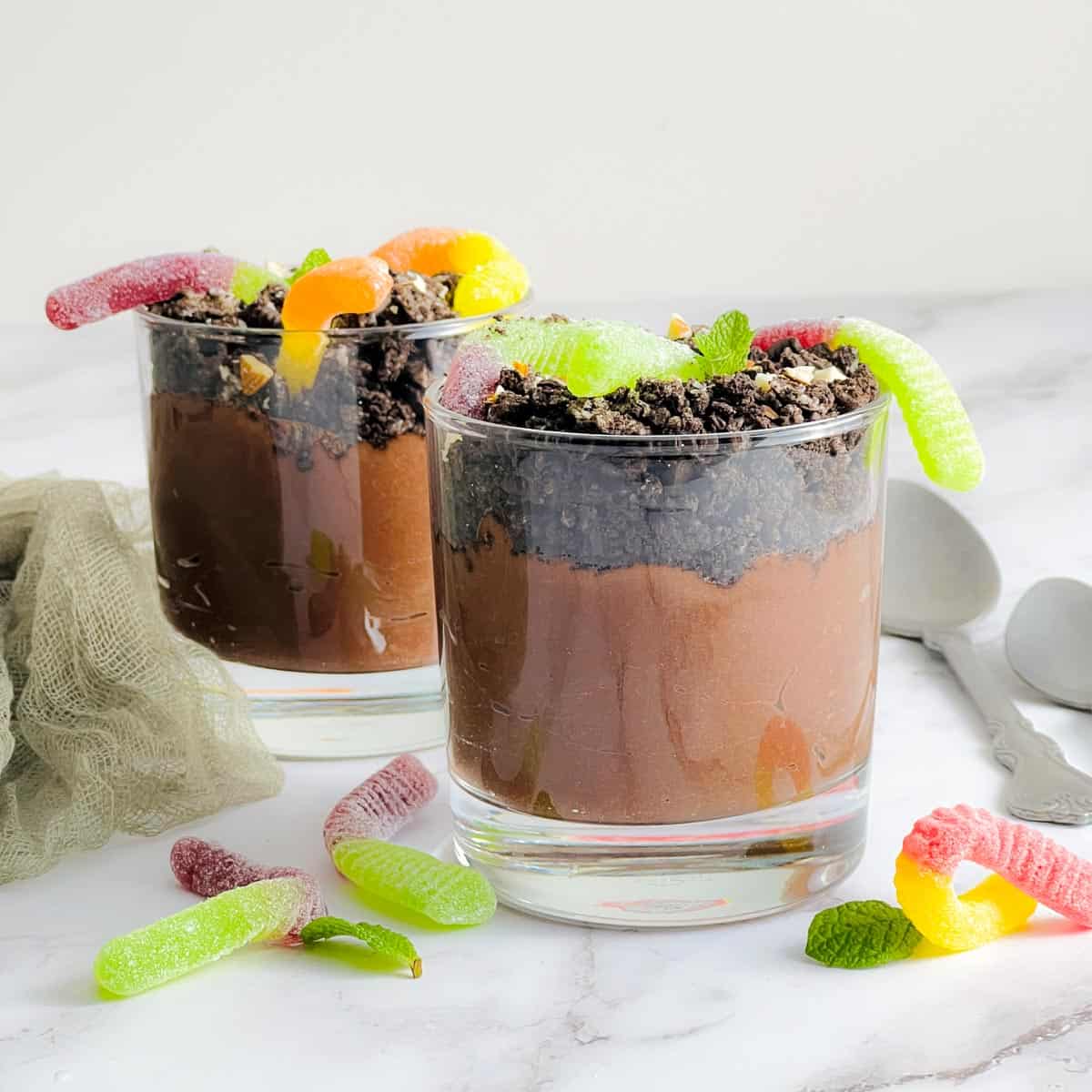 Chocolate dirt pudding with gummy worms and spoons in the background.